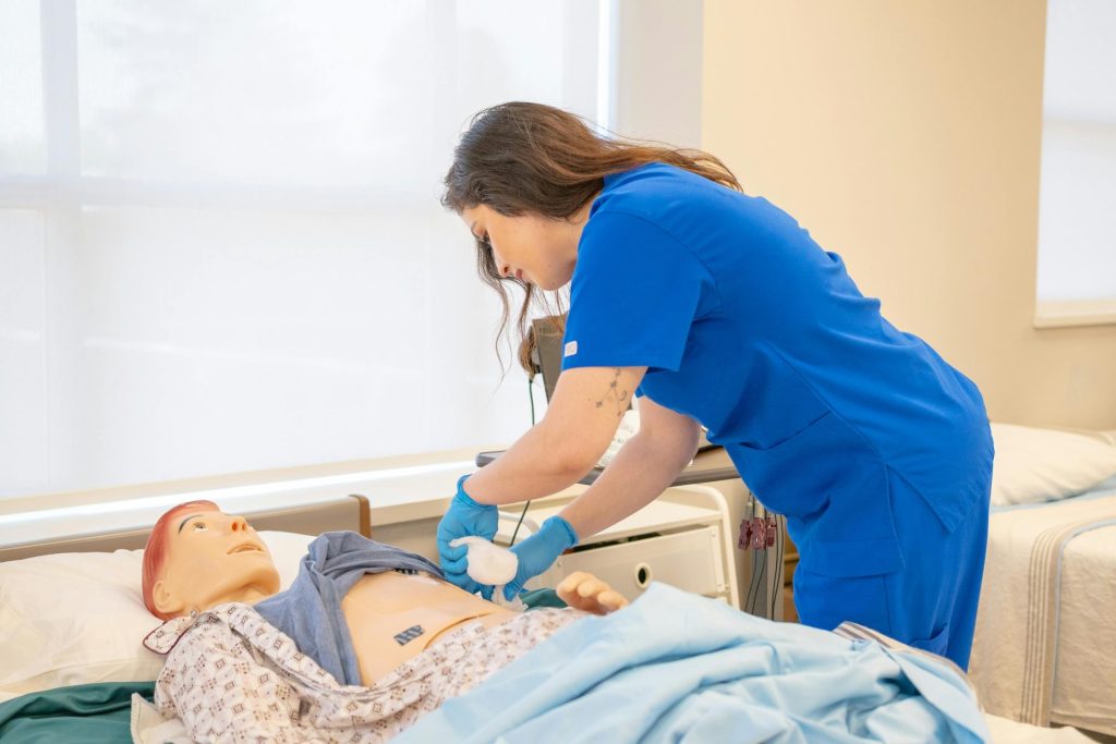 Eine Krankenschwester in blauer OP-Kleidung übt medizinische Eingriffe an einer Krankenhaus-Übungspuppe.